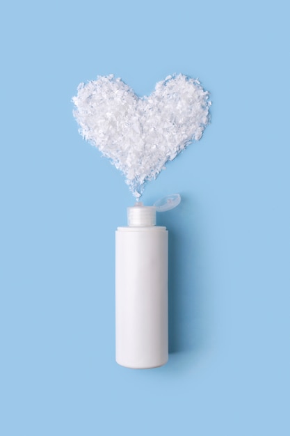 Photo mousse nettoyante dans une bouteille avec coeur de neige sur table bleue