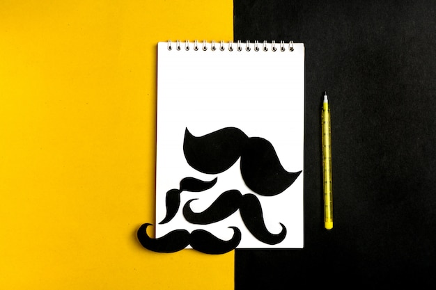 Moustache de papier noir, bloc-notes, stylo, fond jaune