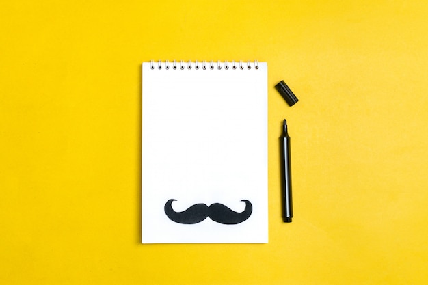 Moustache de papier noir, chapeau, lunettes, bloc-notes sur fond jaune Mois dons, concept de la fête des pères