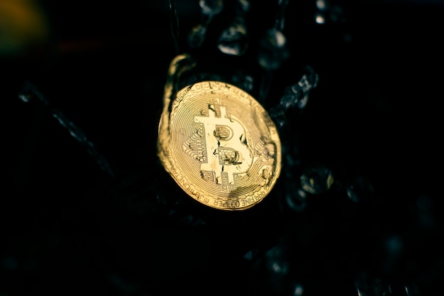 Mouvement de bitcoin doré tomber dans l'eau avec les éclaboussures d'eau sur fond noir, concept de technologie de crypto-monnaie et de technologie blockchain