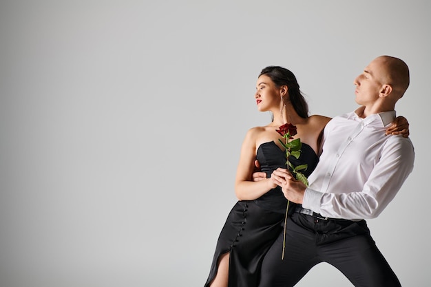 Mouvement de danse dramatique d'un jeune couple femme tenant une rose rouge et homme en tenue formelle en studio