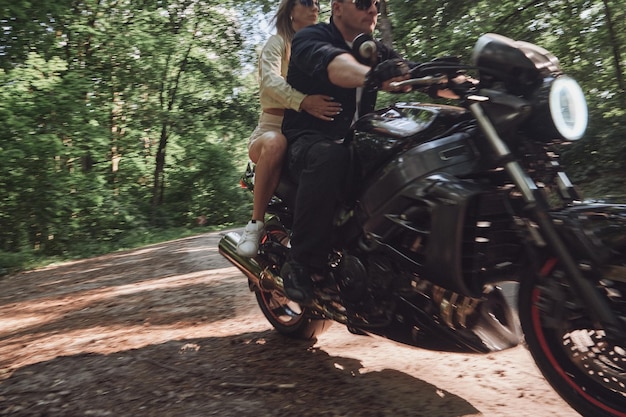 Mouvement flou Un jeune couple heureux conduit une moto sur une route goudronnée dans la liberté de la forêt et la vitesse en mouvement