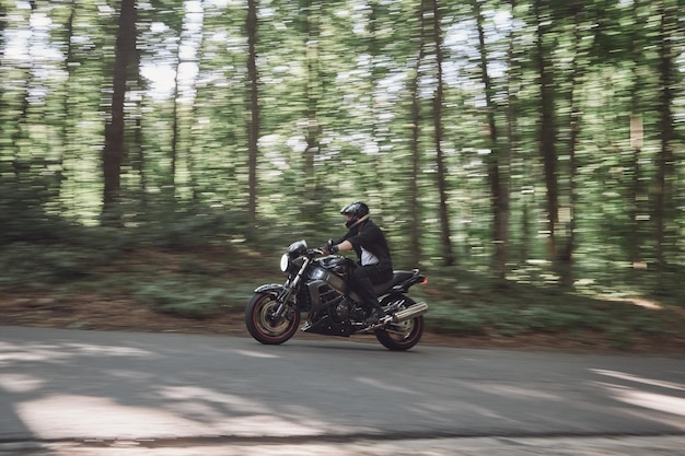 Mouvement flou un jeune motard dans un casque roule rapidement à grande vitesse sur une route forestière en mouvement