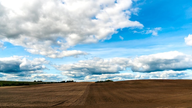 Le mouvement des nuages lors d'une journée d'été ensoleillée sur les champs agricoles Un beau champ vallonné labouré avant de semer diverses céréales blé et seigle