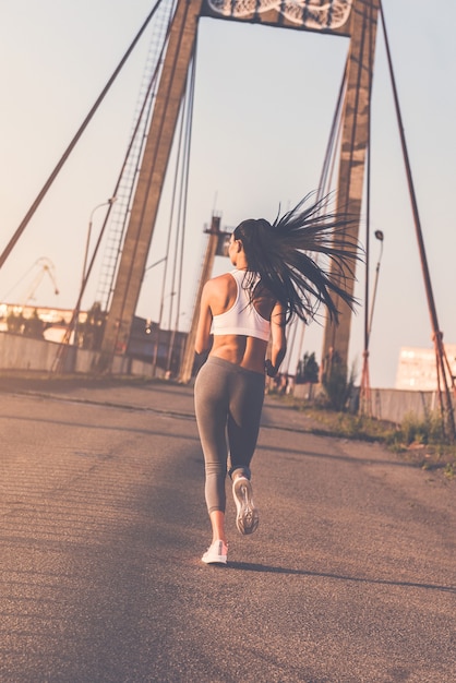 En mouvement. Vue arrière sur toute la longueur de la belle jeune femme en vêtements de sport