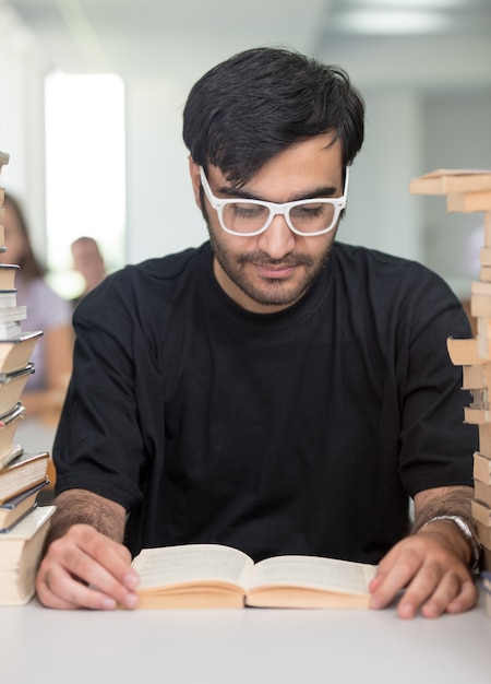 Moyen-oriental jeune étudiant dans la bibliothèque du Collège avec une pile de livres