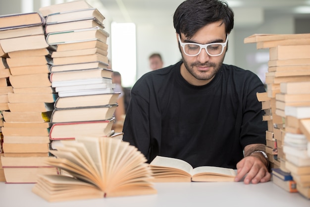 Moyen-oriental jeune étudiant dans la bibliothèque du Collège avec une pile de livres