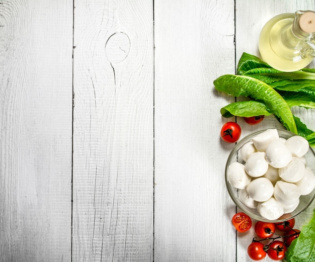 Mozzarella fraîche avec de l'huile d'olive, des tomates et des herbes sur un fond en bois blanc