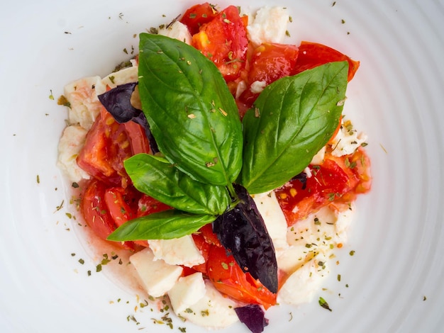 Mozzarella et tomate avec des feuilles de basilic sur fond blanc