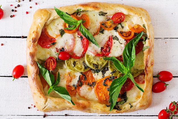 Mozzarella, tomates, tarte salée au basilic sur une table en bois blanc. Nourriture délicieuse, apéritif dans un style méditerranéen. Vue de dessus. Mise à plat