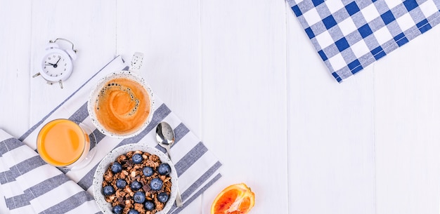 Muesli Aux Bleuets Dans Une Tasse, Jus D'orange Et Café Aromatique Du Matin. Petit Déjeuner Sur Un Fond En Bois Blanc Et Un Réveil. Lay Plat. Espace De Copie