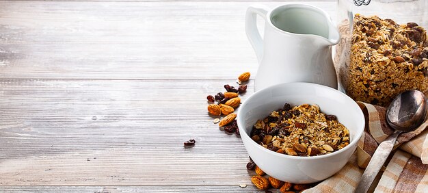 Muesli dans le bol, pot et pichet avec du lait sur la table en bois.