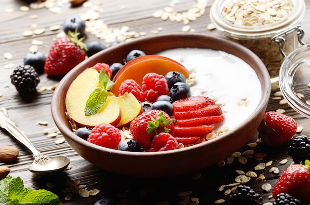 Muesli sain aux fruits avec des pêches, des fraises, des amandes et des mûres dans un plat en argile avec du yaourt sur une table de cuisine en bois