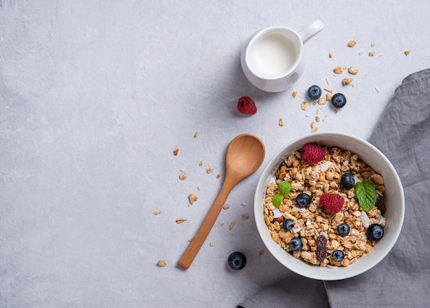 Muesli sucré avec des baies en plaque avec du lait de coco sur table grise.