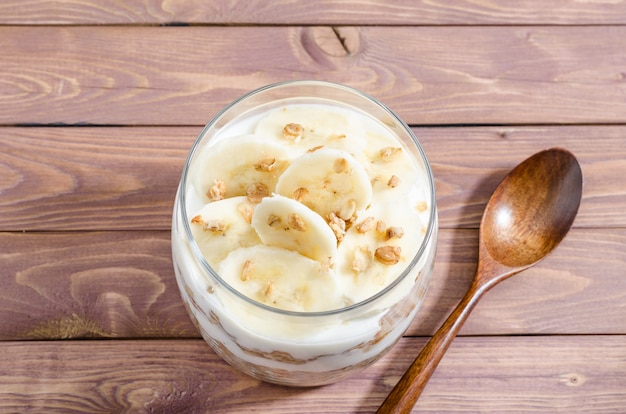 Muesli avec yaourt naturel, banane, noix et fruits secs dans un bocal en verre