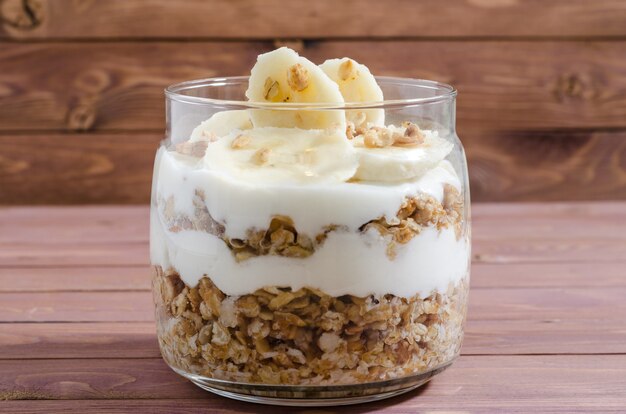 Muesli avec yaourt naturel, banane, noix et fruits secs dans un bocal en verre