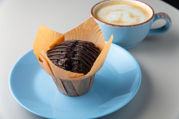 Muffin au chocolat sur plaque bleue et tasse de cappuccino