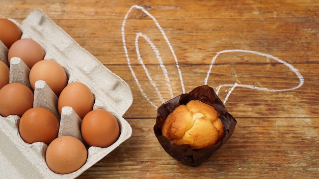 Muffin fait maison avec des oreilles de lapin peintes. Muffin et œufs sur une surface en bois.