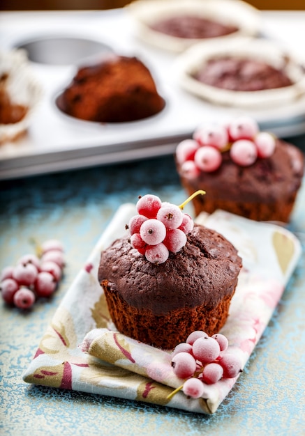 Muffins au chocolat cuits au four, avec baies de branche congelées, groseille rouge, textile bleu, table en bois