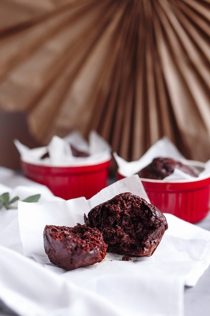 Muffins au chocolat dans des tasses rouges. Petit ramequin en céramique émaillée à gâteaux marron sur fond gris et blanc.