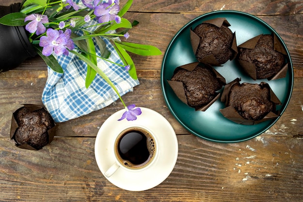 muffins au chocolat faits maison ou madeleine dans une assiette verte avec une tasse de café et un pot de fleurs violettes