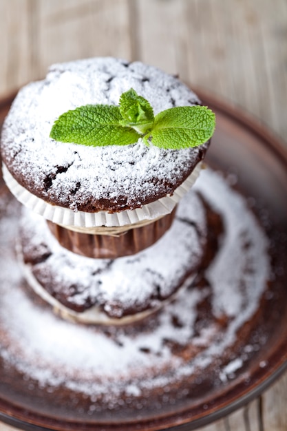 Muffins au chocolat frais avec du sucre en poudre et une feuille de menthe sur une plaque brune sur une table en bois rustique