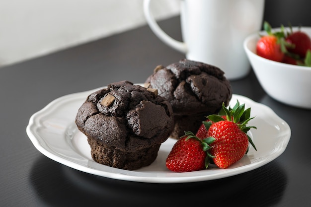 Photo muffins au chocolat et fraises fraîches sur une plaque blanche