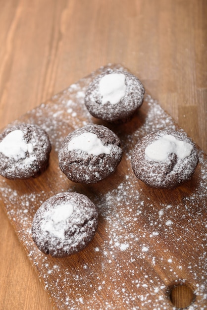 Muffins au chocolat avec glaçage blanc allongé sur une planche saupoudrée de sucre en poudre