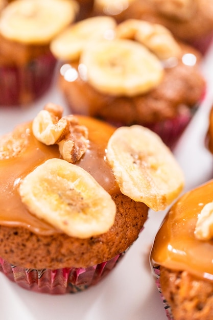 Muffins au pain aux bananes et aux noix fraîchement cuits arrosés de caramel maison, décorés de noix et de chips de banane.