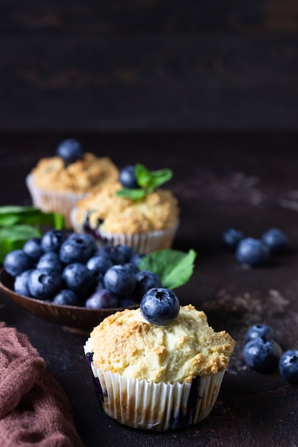 Muffins aux bleuets avec des baies fraîches et des feuilles de menthe sur pierre brune foncée.