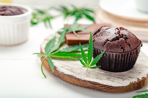 Muffins aux mauvaises herbes avec du cannabis sur le dessus Le cannabis laisse des branches de chanvre sur une table blanche Muffins au cupcake au chocolat à la marijuana avec de l'herbe CBD Médicaments de chanvre de marijuana dans l'espace de copie de dessert