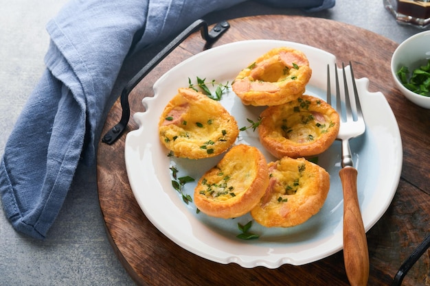 Muffins aux œufs avec oignons verts, bacon, fromage et tomates sur une plaque blanche sur fond clair Petit-déjeuner sain à haute teneur en protéines et faible en glucides prêt à manger