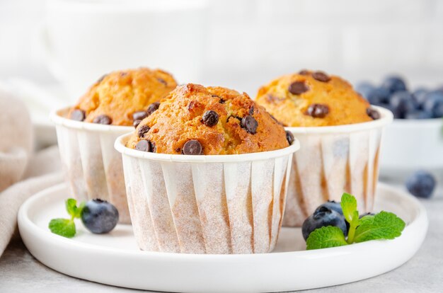 Photo muffins aux pépites de chocolat sur une plaque blanche avec une tasse de café et des bleuets frais sur un fond de béton gris. espace de copie.