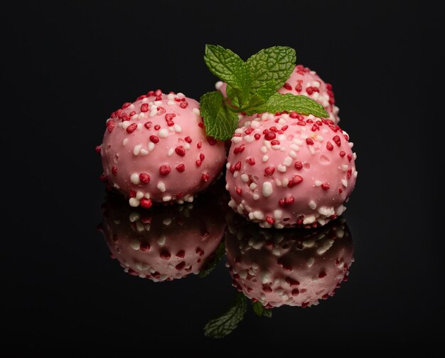 Muffins biscuits ronds roses saupoudrés de glaçage posés sur une surface noire avec un reflet sur fond noir avec des feuilles de menthe