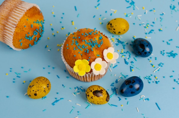 Muffins décorés avec des pépites, des fleurs de mastic et des œufs de caille de Pâques jaunes et bleus