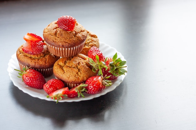 muffins faits maison avec des fraises fraîches sur une plaque blanche sur un tableau noir