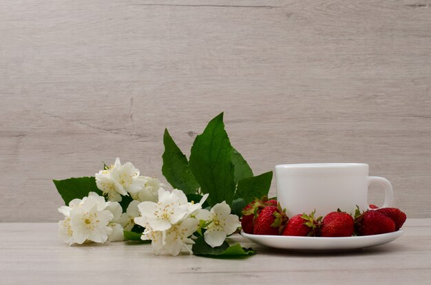 Mug blanc, fleurs de jasmin et fraises sur fond de bois