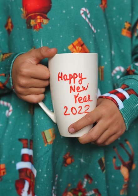 Mug blanc avec l'inscription Nouvel An 2022 dans les mains des enfants, l'enfant porte un sweat-shirt du Nouvel An