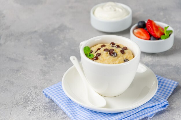 Mug cake aux pépites de chocolat, baies fraîches et crème sur fond de béton gris Espace de copie