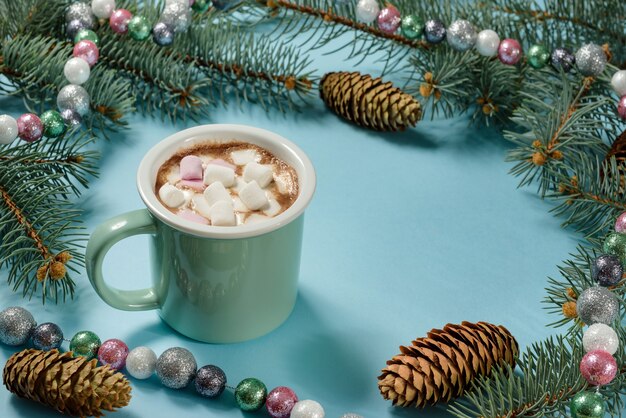 Un mug avec chocolat chaud et guimauves, décoré de branches de sapin, de guirlandes et de perles.