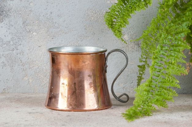 Mug en cuivre antique et plante verte sur une table en béton.