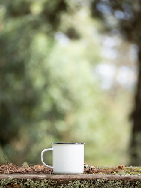 Mug en émail blanc isolé sur une table en bois Boisson chauffante à l'extérieur dans la forêt Concept d'équipement de camping à l'extérieur