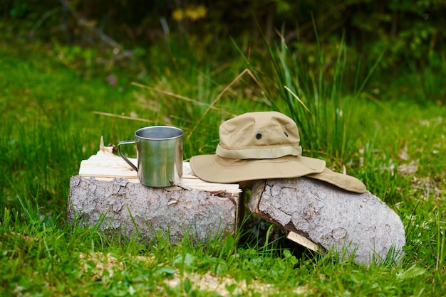 mug en métal et chapeau de touriste avec des champs se trouvent sur un rondin