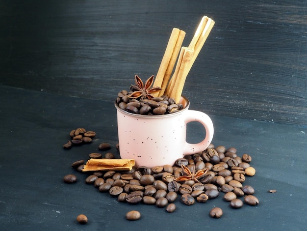 Mug rose avec des grains de café cannelle et anis étoilé isolé sur fond vintage noir