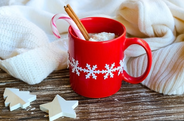 Mug rouge de chocolat chaud avec bâton de cannelle et canne à sucre, chandail tricoté confortable blanc dans le dos. Délicieuse boisson par temps froid. Temps d'hiver ou concept de matin de Noël.
