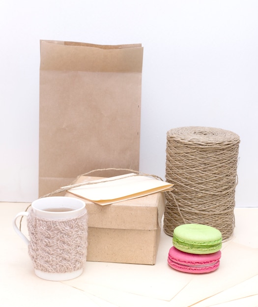 Mug tricoté, macarons colorés et boîte en carton sur sac en papier