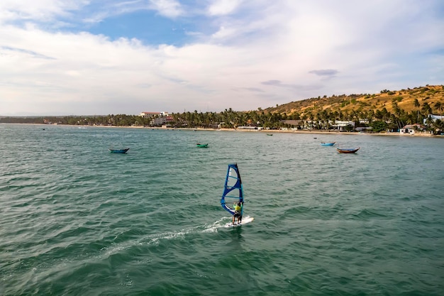 Mui Né, Vietnam. L'homme joue à la planche à voile dans la mer sous un vaste ciel bleu.