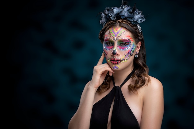 Mujer con maquillaje de catrina tradicional por dia de muertos y usando un vestido negro con fondo