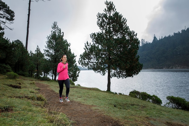 Mujer latina Atleta corriendo al aire libre cerca de un lago con montanas al fondo