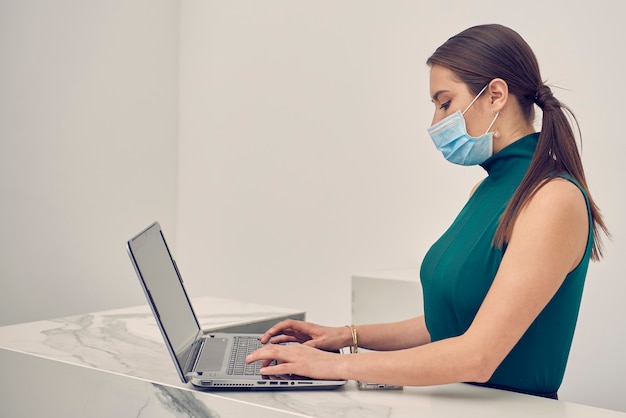 mujer latina con cubrebocas trabajando en su laptop en la recepcion